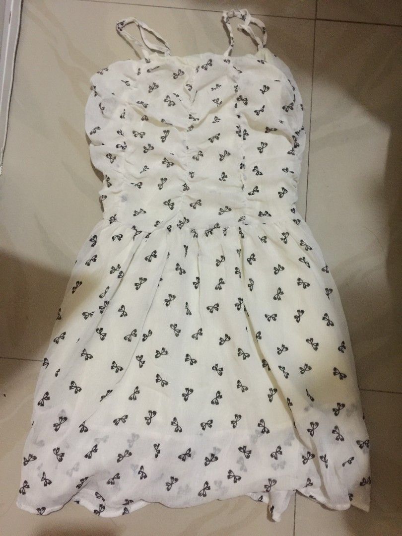 White bow print spaghetti strap sundress (Category: Dresses) located in Marikina City. Submitted by sunflora.thrift (Listing ID 1471084354, Image 1). Description: - Color/Pattern: White with all-over black bow print - Style: Midi length flare silhouette with a sweet ruffle hem - Material: Lightweight chiffon-like fabric with full inner lining - Details: Adjustable thin straps and flattering ruched bust detailing - Condition: Brand new / Excellent