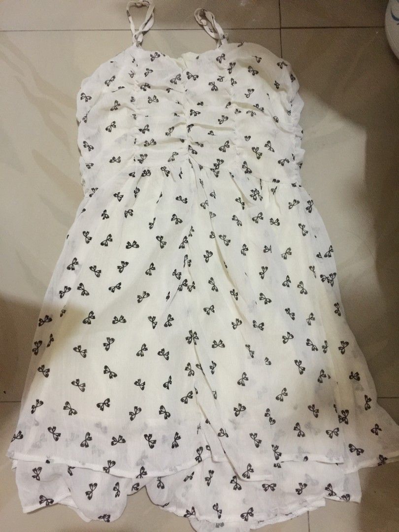 White bow print spaghetti strap sundress (Category: Dresses) located in Marikina City. Submitted by sunflora.thrift (Listing ID 1471084354, Image 3). Description: - Color/Pattern: White with all-over black bow print - Style: Midi length flare silhouette with a sweet ruffle hem - Material: Lightweight chiffon-like fabric with full inner lining - Details: Adjustable thin straps and flattering ruched bust detailing - Condition: Brand new / Excellent