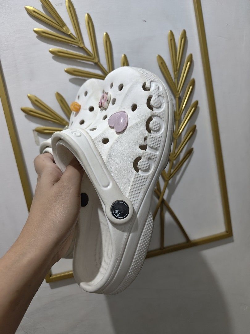 White Crocs Classic Clogs with Jibbitz Charms W7 (Category: Slippers and slides) located in Mandaluyong City. Submitted by declutterpreloved2.0 (Listing ID 1471087804, Image 2). Description: - Color: Classic White - Style: Slip-on clogs with pivoting heel straps - Included Jibbitz: Pink heart, Kitty donut, orange flower, and sparkly rectangular charm - Condition: Normal signs of wear on soles and uppers - Features: Super comfortable, perfect for 