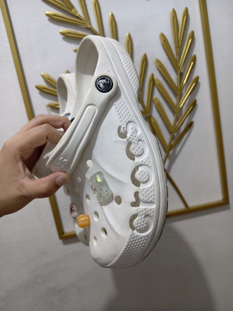 White Crocs Classic Clogs with Jibbitz Charms W7 (Category: Slippers and slides) located in Mandaluyong City. Submitted by declutterpreloved2.0 (Listing ID 1471087804, Image 3). Description: - Color: Classic White - Style: Slip-on clogs with pivoting heel straps - Included Jibbitz: Pink heart, Kitty donut, orange flower, and sparkly rectangular charm - Condition: Normal signs of wear on soles and uppers - Features: Super comfortable, perfect for 