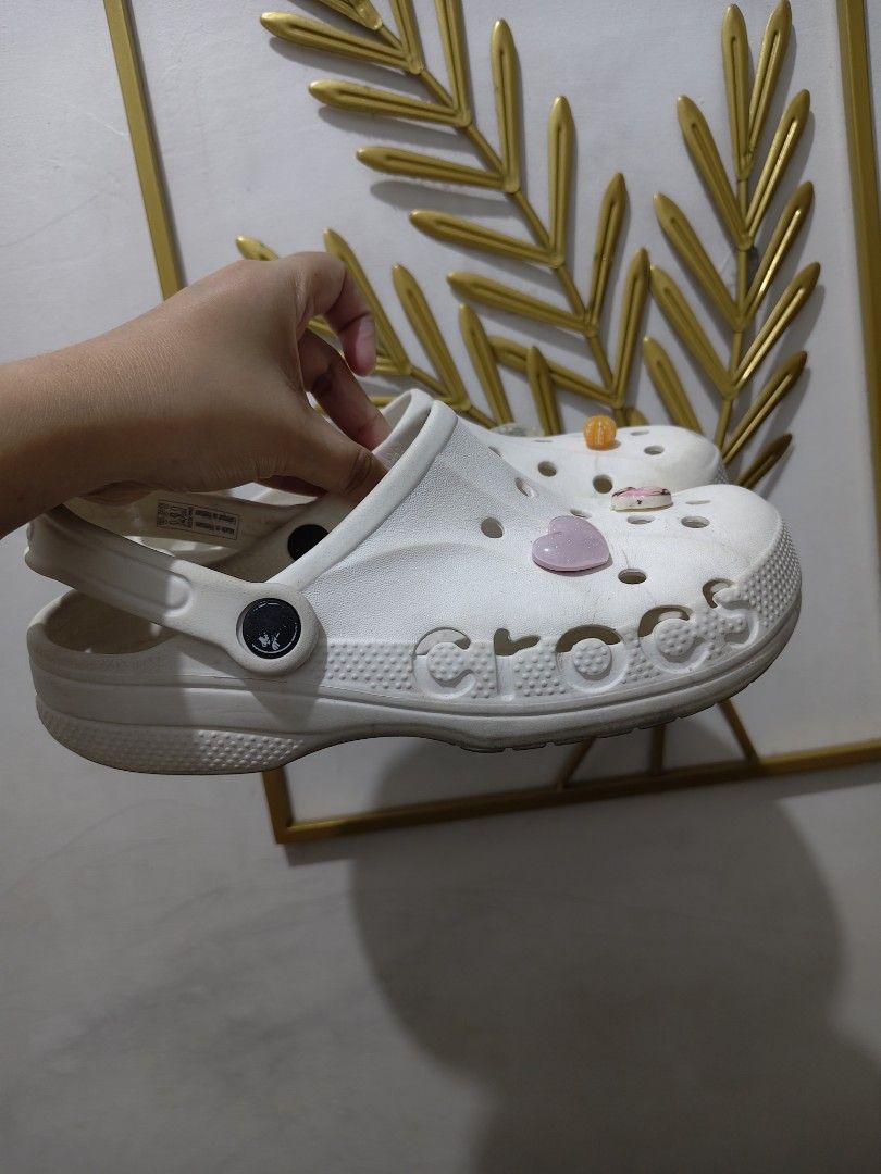 White Crocs Classic Clogs with Jibbitz Charms W7 (Category: Slippers and slides) located in Mandaluyong City. Submitted by declutterpreloved2.0 (Listing ID 1471087804, Image 1). Description: - Color: Classic White - Style: Slip-on clogs with pivoting heel straps - Included Jibbitz: Pink heart, Kitty donut, orange flower, and sparkly rectangular charm - Condition: Normal signs of wear on soles and uppers - Features: Super comfortable, perfect for 