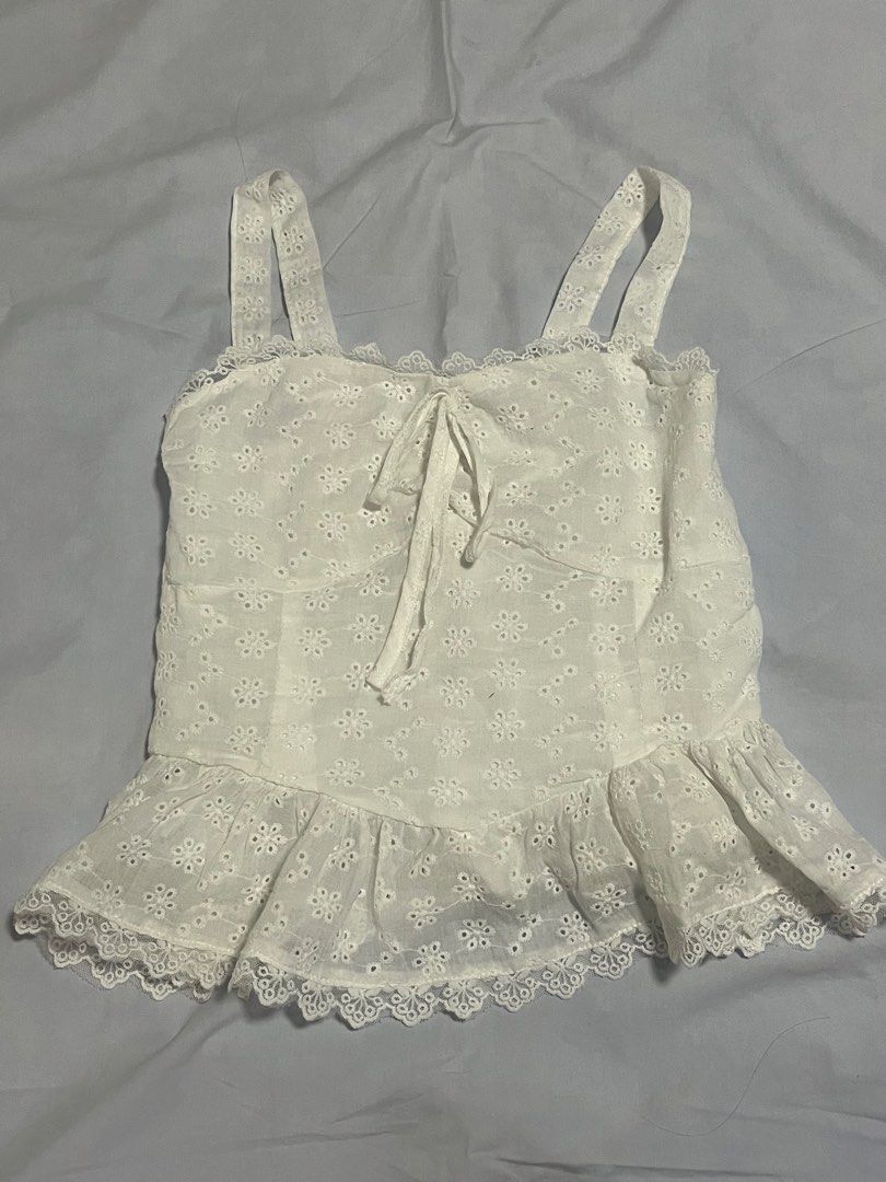 White eyelet lace cami top with ruffle hem (Category: Sleeveless) located in Manila. Submitted by aaa0ki (Listing ID 1470956495, Image 1). Description: - Color: White - Material/Pattern: Floral eyelet lace cut-out fabric - Neckline: Square neck with front tie detail - Straps: Comfortable wide shoulder straps - Fit: Smocked stretchy back panel for easy fit - Hem: Flared ruffle hem with scalloped lace trim - Condition: Brand new / Excellent (ready 