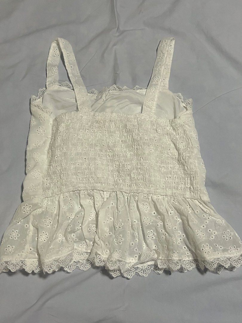 White eyelet lace cami top with ruffle hem (Category: Sleeveless) located in Manila. Submitted by aaa0ki (Listing ID 1470956495, Image 2). Description: - Color: White - Material/Pattern: Floral eyelet lace cut-out fabric - Neckline: Square neck with front tie detail - Straps: Comfortable wide shoulder straps - Fit: Smocked stretchy back panel for easy fit - Hem: Flared ruffle hem with scalloped lace trim - Condition: Brand new / Excellent (ready 