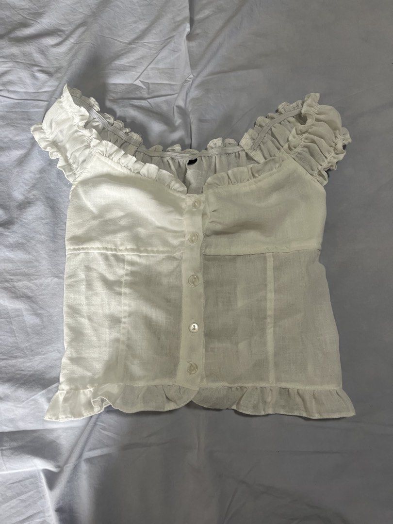 White off-shoulder ruffled button-down cropped blouse (Category: Blouses) located in Manila. Submitted by aaa0ki (Listing ID 1470956465, Image 1). Description: - Color: White - Style: Off-shoulder crop top with square neckline - Details: Short ruffled sleeves, front button-down design with 5 buttons, and a playful ruffle hem - Fit: Stretchy smocked back panel for a comfortable and flattering fit - Fabric: Lightweight and breathable - Pairing: Loo