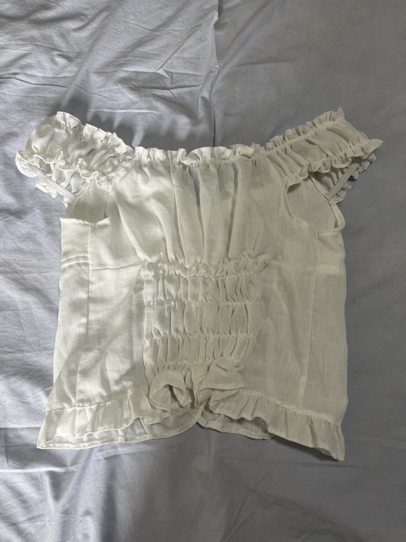 White off-shoulder ruffled button-down cropped blouse (Category: Blouses) located in Manila. Submitted by aaa0ki (Listing ID 1470956465, Image 2). Description: - Color: White - Style: Off-shoulder crop top with square neckline - Details: Short ruffled sleeves, front button-down design with 5 buttons, and a playful ruffle hem - Fit: Stretchy smocked back panel for a comfortable and flattering fit - Fabric: Lightweight and breathable - Pairing: Loo