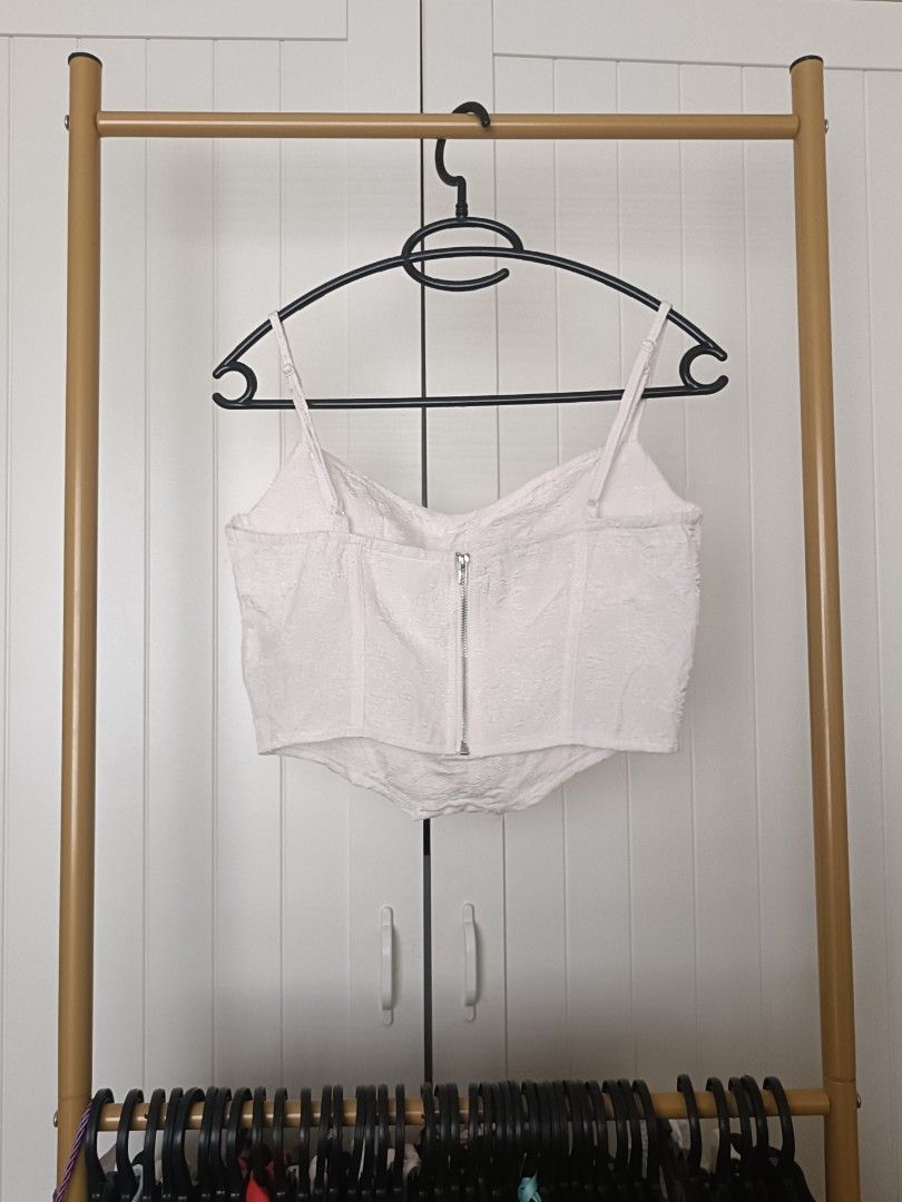 White textured corset crop top (Category: Sleeveless) located in Bacoor. Submitted by Miss_Chuch0521 (Listing ID 1470963290, Image 2). Description: - Color: White with subtle textured floral pattern - Style: Corset-style crop top with structured boning for a fitted shape - Neckline & Straps: Cowl neckline with thin adjustable spaghetti straps - Closure: Exposed silver zipper down the back - Pairing: Looks great with high-waisted denim jeans.