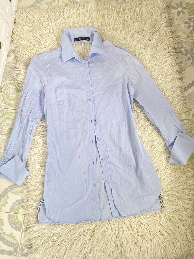 Zara Basic Light Blue Long Sleeve Button Up Shirt (Category: Longsleeves) located in Tabaco. Submitted by camila_p (Listing ID 1470986800, Image 1). Description: - Brand: Zara Basic - Color: Light Blue - Size: S - Style: Long sleeve button-up with classic collar and front button closure - Design Details: Wide cuffs and unique open-back wrap detail - Versatility: Great for layering or solo wear - Condition: Clean with light wrinkling from storage.
