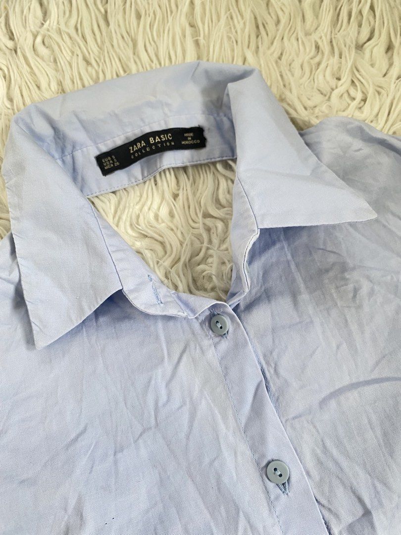 Zara Basic Light Blue Long Sleeve Button Up Shirt (Category: Longsleeves) located in Tabaco. Submitted by camila_p (Listing ID 1470986800, Image 2). Description: - Brand: Zara Basic - Color: Light Blue - Size: S - Style: Long sleeve button-up with classic collar and front button closure - Design Details: Wide cuffs and unique open-back wrap detail - Versatility: Great for layering or solo wear - Condition: Clean with light wrinkling from storage.