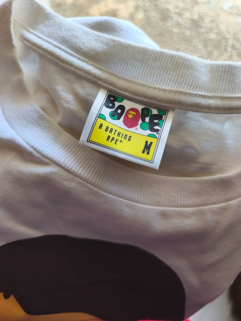 A Bathing Ape BAPE Ape Head White T-Shirt (Category: Tshirts & Polo Shirts ) located in Caloocan City. Submitted by neiledrian (Listing ID 1465727255, Image 1). Description: - Brand: A Bathing Ape (BAPE) - Color: Classic White - Design: Large brown and gold ape head print on the front - Size: Medium - Material: 100% cotton - Details: Yellow neck tag and standard interior wash tag included.