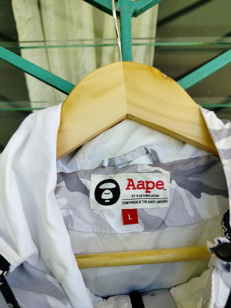 Aape By A Bathing Ape Camo Anorak Jacket Size L (Category: Coats, Jackets and Outerwear) located in Manila. Submitted by virgiliosa38485 (Listing ID 1465706251, Image 2). Description: - Brand: Aape - Style: White and grey camouflage anorak jacket - Size: Large (L) -Dimes 29×23.5 - Design: Bold 'AAPE NOW' block lettering on the front placket - Features: Drawstring hood with branded aglets, front kangaroo pocket, and secure side zip pockets - Detai