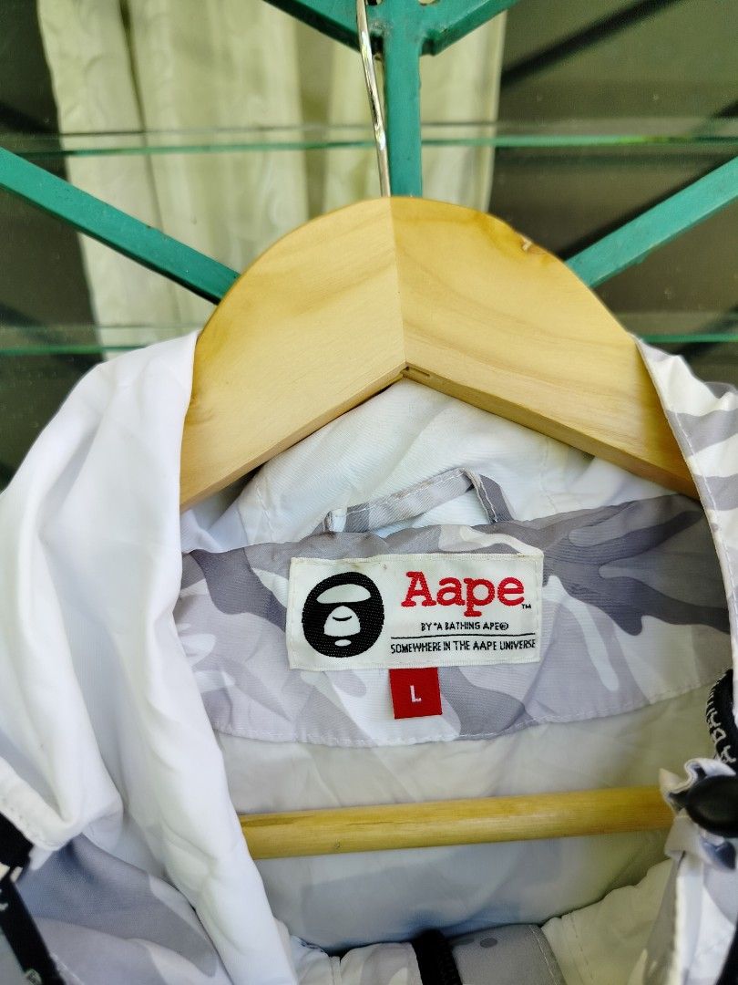 Aape By A Bathing Ape Camo Windbreaker Jacket (Category: Coats, Jackets and Outerwear) located in Manila. Submitted by gerald_quinto (Listing ID 1465708164, Image 2). Description: - Brand: Aape by A Bathing Ape - Style: Grey and white camo half-zip pullover windbreaker - Size: Large -Dimes 29×23.5 - Features: Adjustable hood, front pocket, and large 'Aape Now' front placket branding - Details: Contrast white lower panel with logo graphic, plus em