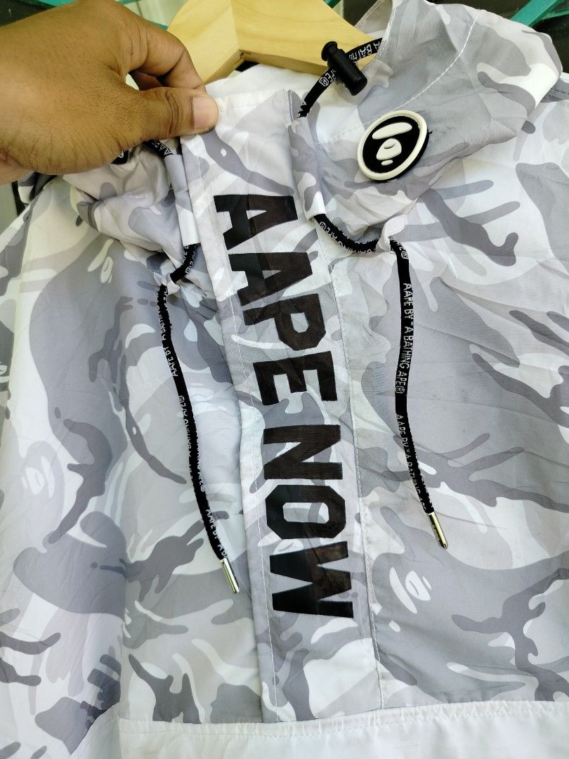 Aape By A Bathing Ape Camo Windbreaker Jacket (Category: Coats, Jackets and Outerwear) located in Manila. Submitted by gerald_quinto (Listing ID 1465708164, Image 3). Description: - Brand: Aape by A Bathing Ape - Style: Grey and white camo half-zip pullover windbreaker - Size: Large -Dimes 29×23.5 - Features: Adjustable hood, front pocket, and large 'Aape Now' front placket branding - Details: Contrast white lower panel with logo graphic, plus em