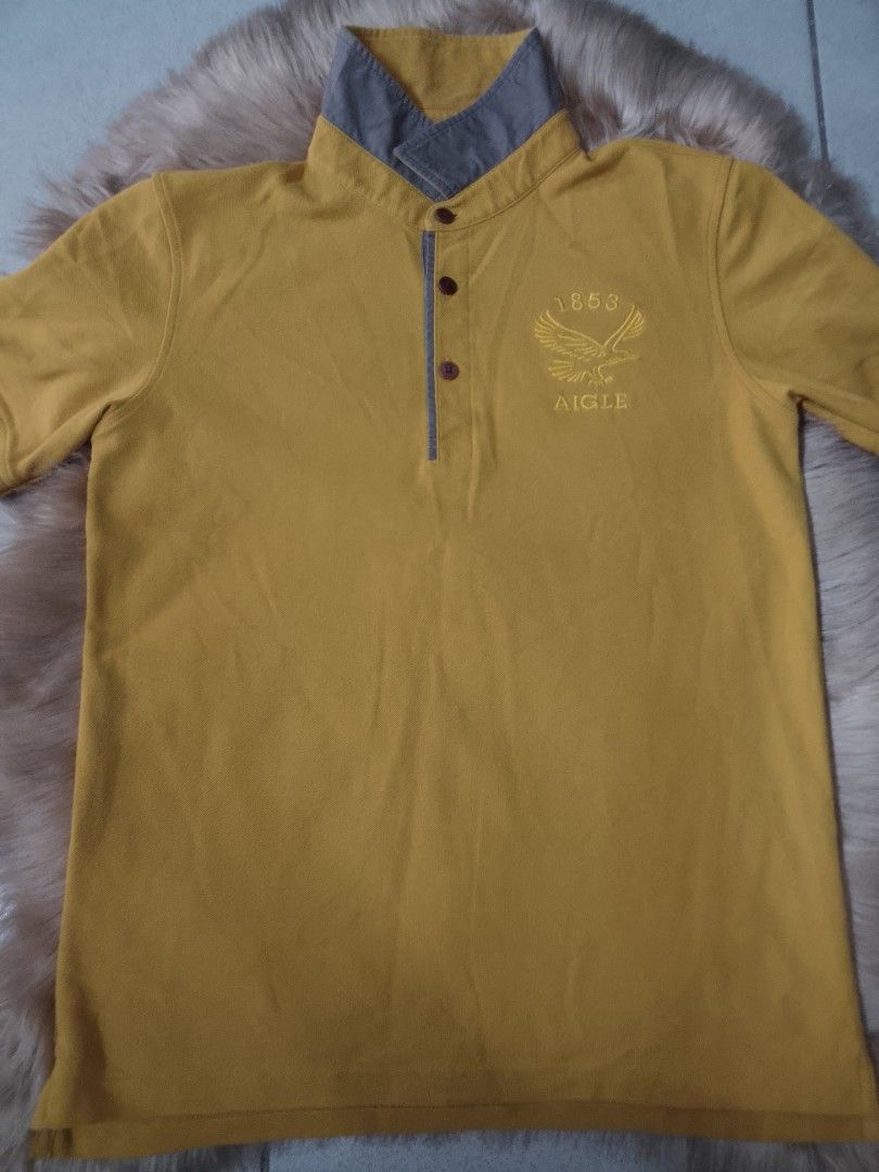 Aigle CT115 "EAGLETWIST" POLO SHIRT (Category: Tshirts & Polo Shirts ) located in Manila. Submitted by jctclthng_2026 (Listing ID 1465622683, Image 1). Description: - Brand: Aigle (Est. 1853) - Color: Mustard yellow with contrasting grey inner collar and placket - Material: Classic pique cotton fabric - Details: Three dark brown branded buttons, embroidered eagle logo on the left chest - Fit: Short sleeves, standard hem - Condition: Clean, well-m