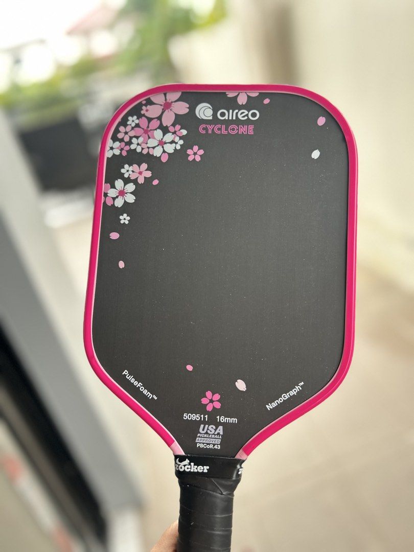 Aireo Cyclone 16mm Pickleball Paddle (Category: Racket and Ball Sports) located in Binan City. Submitted by guiltfreefashion (Listing ID 1465587561, Image 1). Description: - Brand/Model: Aireo Cyclone Pickleball Paddle - Core Thickness: 16mm for optimal control and power - Design: Sleek black face with pink cherry blossom graphics and bright pink edge guard - Technologies: Built with PulseFoam and NanoGraph tech - Certification: USA Pickleball ap