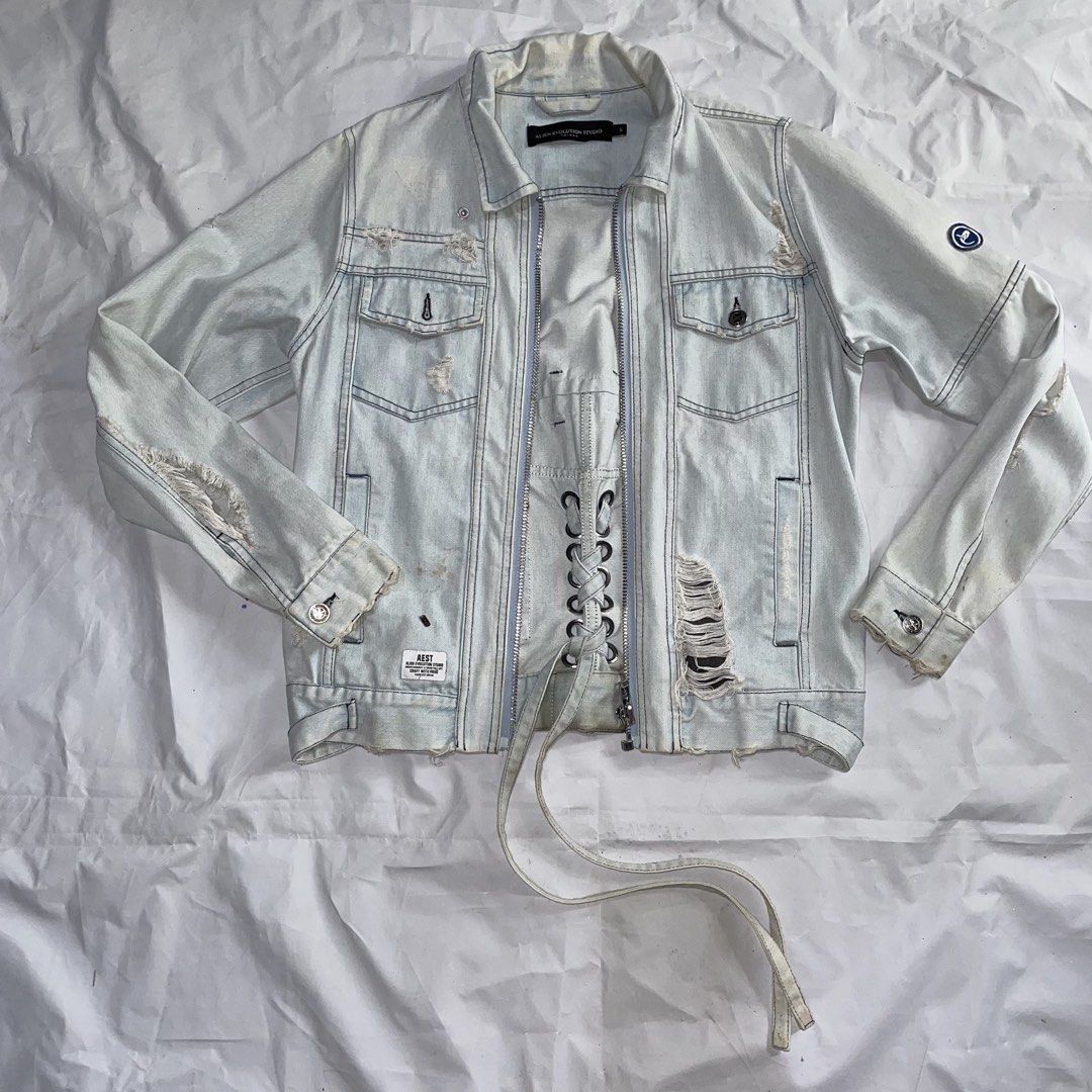 Alien Evolution Studio Distressed Denim Jacket Size S (Category: Coats, Jackets and Outerwear) located in La Trinidad. Submitted by ukaynirey (Listing ID 1465692904, Image 1). Description: Alien Evolution Studio denim jacket in light wash. Size S. Features distressing, zip front, and lace-up corset detail on the lower front. Embroidered patch on the left sleeve. Multiple utility pockets and woven brand patch near the hem. Unique streetwear piece 