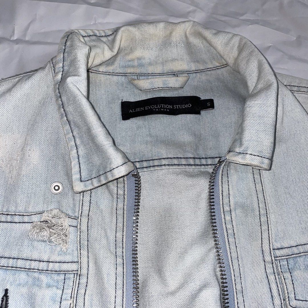 Alien Evolution Studio Distressed Denim Jacket Size S (Category: Coats, Jackets and Outerwear) located in La Trinidad. Submitted by ukaynirey (Listing ID 1465692904, Image 2). Description: Alien Evolution Studio denim jacket in light wash. Size S. Features distressing, zip front, and lace-up corset detail on the lower front. Embroidered patch on the left sleeve. Multiple utility pockets and woven brand patch near the hem. Unique streetwear piece 