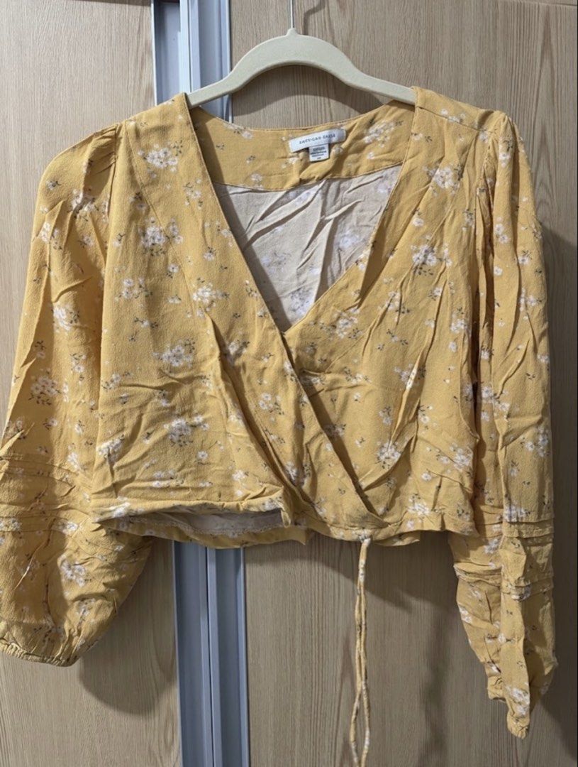 American Eagle Floral Crop Wrap Blouse Yellow (Category: Blouses) located in Taguig. Submitted by gjohnson_ (Listing ID 1465710743, Image 1). Description: - Brand: American Eagle - Size: Medium (tag inside) - Material: Light, breathable fabric (Made in India) - Design: Yellow wrap blouse with white floral print - Details: Long sleeves with ruffled tiers, V-neck wrap front, side tie waist, and cropped length - Condition: Excellent pre-loved condit
