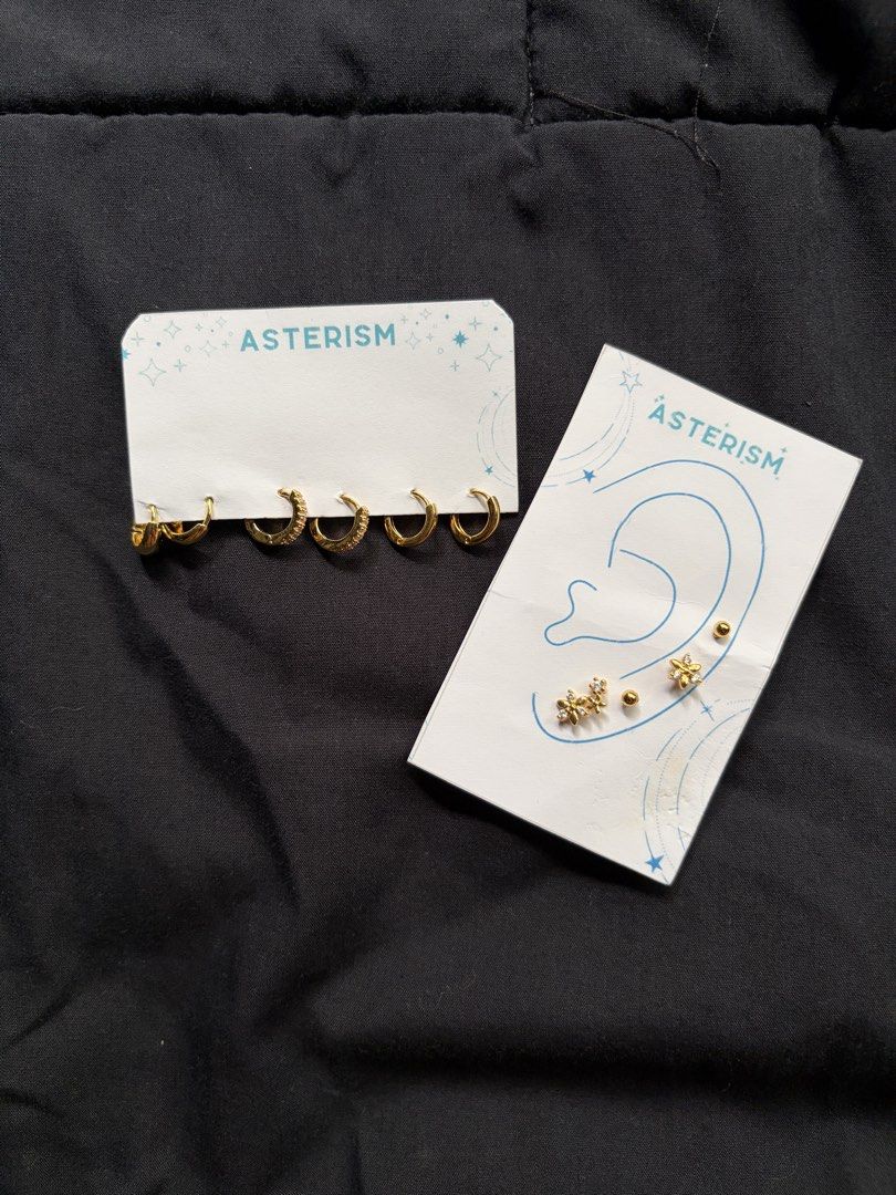 Asterism Gold Earring Sets (Category: Earrings) located in Quezon City. Submitted by katedeclutter (Listing ID 1465594165, Image 1). Description: - Get both earring sets for ₱200! - Brand: Asterism - Condition: Brand new, unworn on original store backing cards - Set 1 (Left Card): 6 gold hoop earrings (mix of plain and crystal-embellished) - Set 2 (Right Card): 5 assorted gold-toned studs and small hoops arranged by ear diagram - Color: Gold-tone