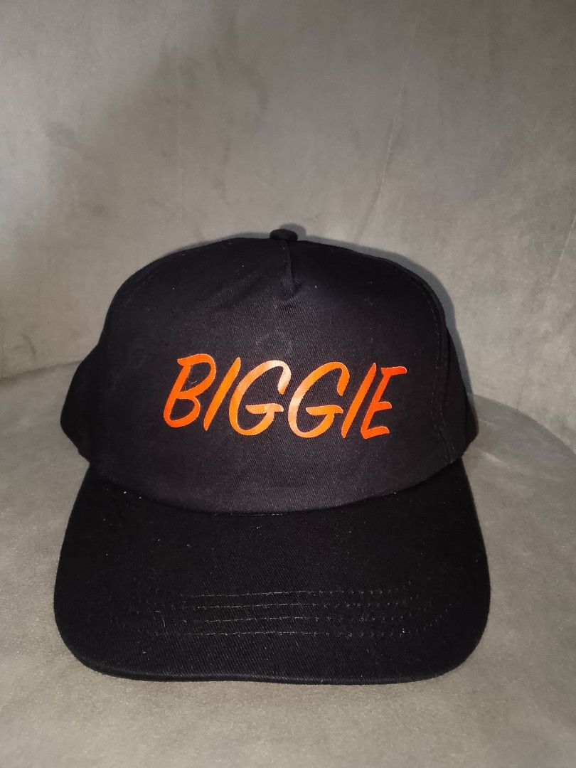 BIGGIE" Black Custom Baseball Hat Cap (Category: Caps & Hats) located in Binangonan. Submitted by yuristalin888 (Listing ID 1465585994, Image 2). Description: * **Design:** Features bold orange embroidered text spelling "BIGGIE" across the front panel. * **Structure:** Classic 5-panel unstructured crown with a solid black fabric body and a curved brim. * **Interior & Details:** Made of 100% cotton with black interior lining and taping. * **Fit:**