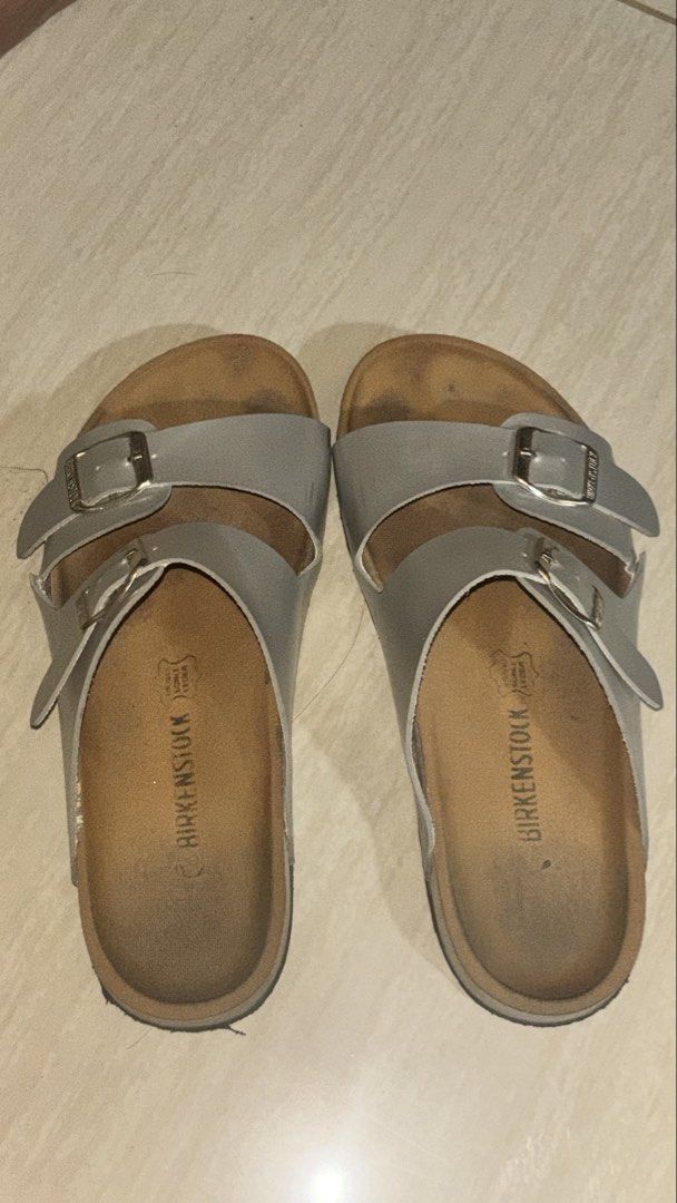 Birkenstock Two-Strap Sandals Silver (Category: Flats & Sandals) located in Manila. Submitted by cheetosjalapeno.f6b498 (Listing ID 1465709859, Image 1). Description: - Authentic silver Birkenstock sandals - Features two adjustable metal buckles with engraved brand name - Classic cork footbed with brand logo stamp - Smooth synthetic upper material - Condition note: Footbed shows noticeable wear and dark discoloration from regular use, but fully f