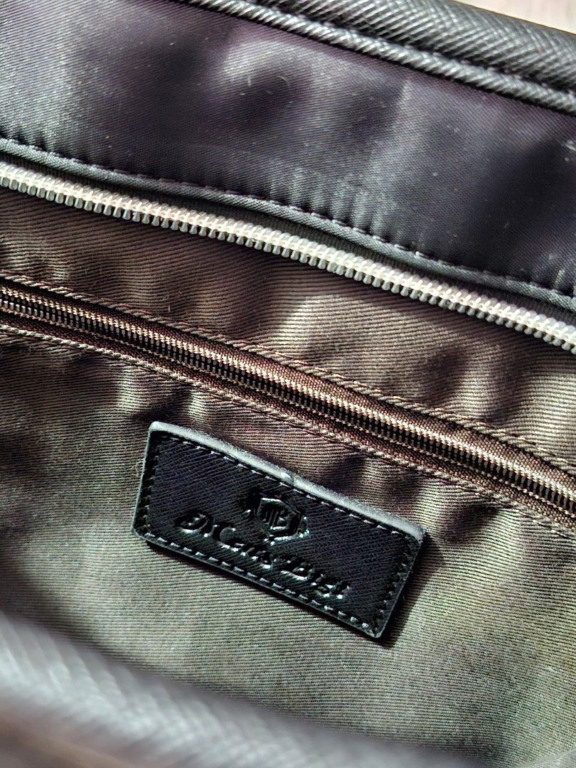Black Nylon Tote Bag (Category: Tote Bags) located in Caloocan City. Submitted by bycara (Listing ID 1465642162, Image 3). Description: Black nylon tote bag with faux leather trim and silver tone hardware. Dual carry handles on top. Front features a vertical zipper pocket, a flap pocket, and a central strap snap closure. Back includes a large open pocket and side zipper expansion. Interior lined in brown fabric with an inner zipped compartment an