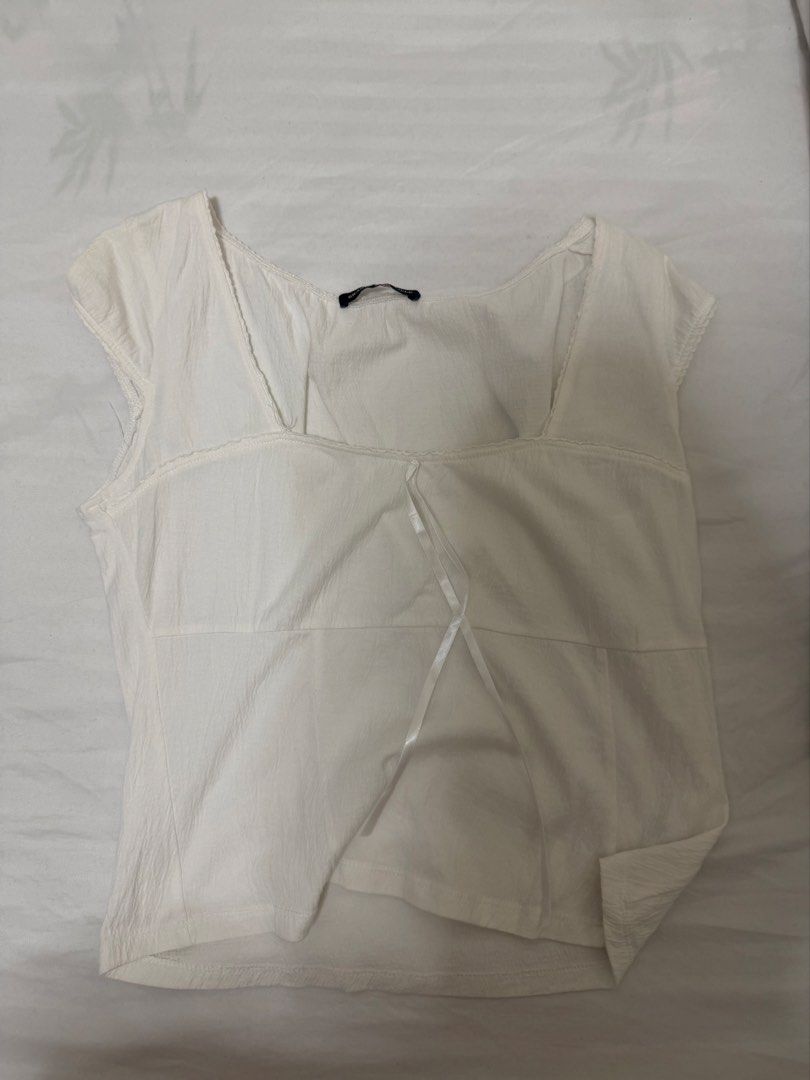 Brandy Melville White Bow Blouse Top (Category: Blouses) located in Santa Rosa. Submitted by decluttering_. (Listing ID 1465623980, Image 1). Description: - Brand: Brandy Melville - Color: White - Details: Square neckline, short cap sleeves, front ribbon tie, lightweight crinkled fabric - Condition: Brand new with tag attached inside collar - Style: Clean, minimalist, and easy to pair with high-waisted jeans or skirts.