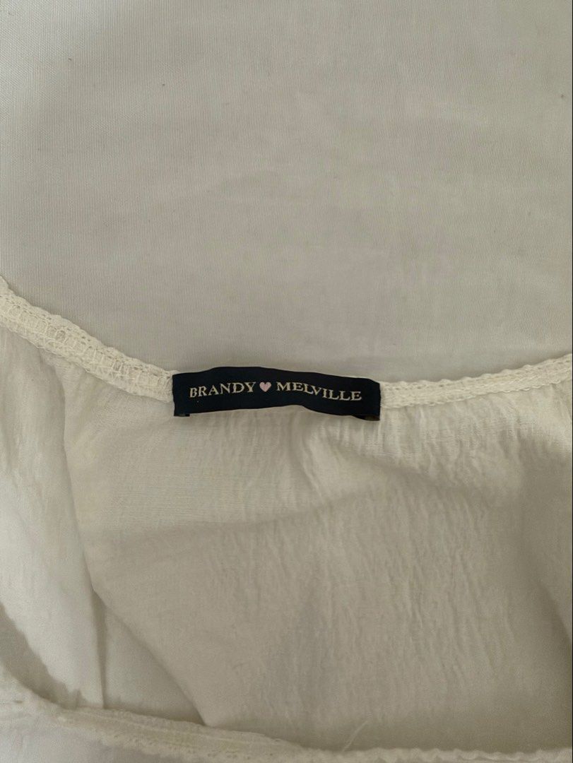 Brandy Melville White Bow Blouse Top (Category: Blouses) located in Santa Rosa. Submitted by decluttering_. (Listing ID 1465623980, Image 3). Description: - Brand: Brandy Melville - Color: White - Details: Square neckline, short cap sleeves, front ribbon tie, lightweight crinkled fabric - Condition: Brand new with tag attached inside collar - Style: Clean, minimalist, and easy to pair with high-waisted jeans or skirts.