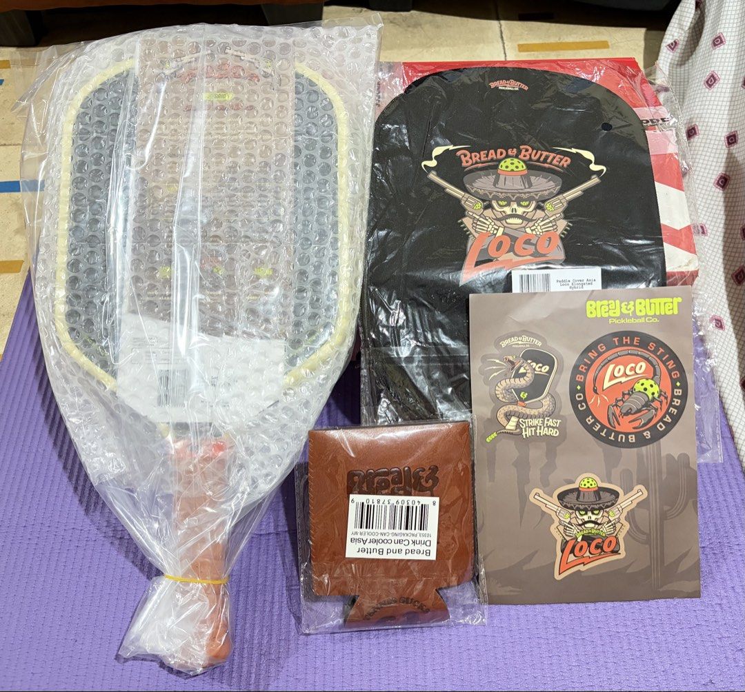 Bread & Butter Loco Pickleball Paddle Bundle (Category: Racket and Ball Sports) located in Manila. Submitted by vn_bmrg (Listing ID 1465709661, Image 1). Description: - Brand: Bread & Butter - Model: Loco hybrid pickleball paddle - Condition: Brand new, sealed in original bubble wrap and plastic packaging - Inclusions: Matching black paddle cover with Loco graphics, sticker sheet, and brown leather-look can cooler - Perfect complete set for playe