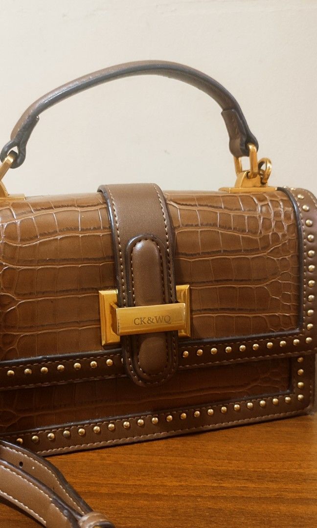 CKWQ Structured Hand bag Sling Bag. (Category: Cross-body Bags) located in Pasig City. Submitted by xcess_baggage (Listing ID 1462054845, Image 2). Description: - Stylish brown handbag with a luxurious crocodile embossed texture. - Eye-catching studded details along the edges for added flair. - Secure and elegant gold buckle closure. - Comfortable top handle for easy carrying. - Includes a detachable crossbody strap for versatile wear. - Practica
