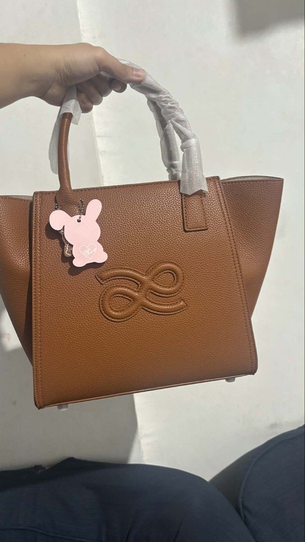 Brown Leather Tote Bag with Handles (Category: Tote Bags) located in Cavite. Submitted by triciajuntilla5 (Listing ID 1465599139, Image 1). Description: - Material: Premium brown pebbled leather with clean stitching - Design: Structured shape with embossed monogram on the front - Handles: Dual top handles still wrapped in protective plastic - Hardware: Protective metal feet on the bottom .