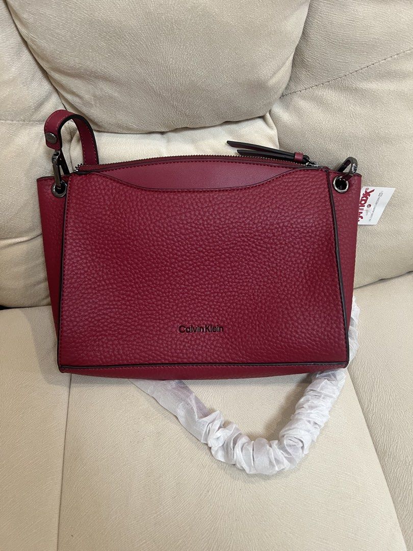 Calvin Klein Red Crossbody Bag (Category: Cross-body Bags) located in Manila. Submitted by pau_only (Listing ID 1465674413, Image 1). Description: - Brand: Calvin Klein - Material: Rich burgundy textured faux leather with dark hardware - Condition: Brand new, stored away with zero wear - Strap: Still wrapped in original packaging, never used - Interior: Dark fabric lining with an extra zip pocket - Closure & Shape: Secure top zip closure with a c
