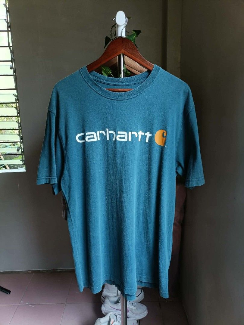Carhartt Teal T-Shirt (Category: Tshirts & Polo Shirts ) located in Manila. Submitted by kiraaaaaaaaaaa (Listing ID 1465593331, Image 1). Description: - Brand: Carhartt - Color: Teal blue with slight vintage fade - Style: Short sleeve crewneck workwear t-shirt - Design: White Carhartt script logo and orange C graphic on chest - Material: Soft cotton fabric - Details: Tag K195, made in Haiti.