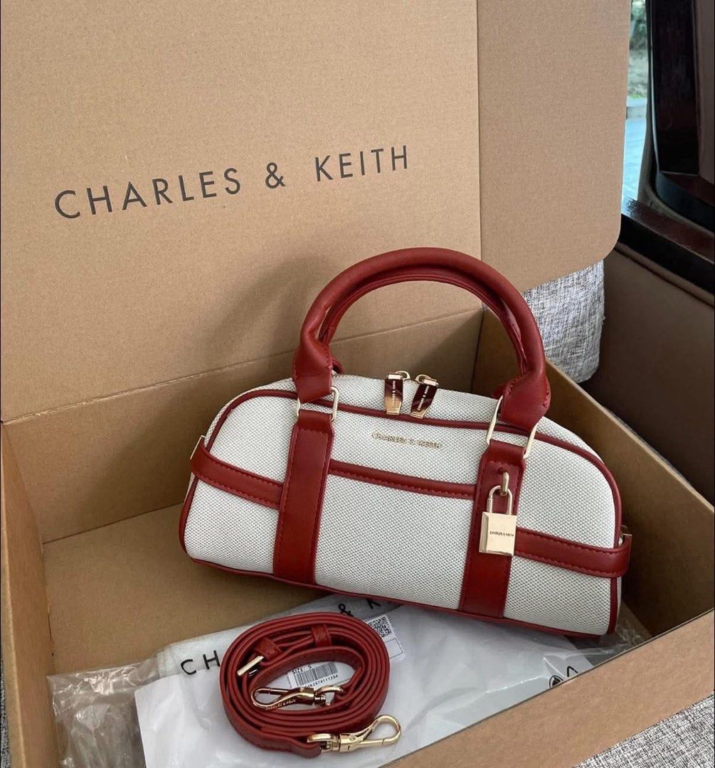 Charles & Keith White and Red Barrel Bag with Lock (Category: Cross-body Bags) located in Pasig City. Submitted by bagsnmore4 (Listing ID 1465580549, Image 1). Description: - Brand: Charles & Keith - Style: Barrel bag in white canvas with striking red trim - Hardware: Gold-tone accents with a chic decorative front padlock - Closure: Secure zip closure - Strap: Matching red adjustable and detachable shoulder strap - Condition: Excellent.