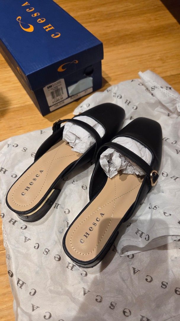 Chesca Black Mules Size 37 (Category: Heels) located in Mandaluyong City. Submitted by loijiminigo (Listing ID 1465655520, Image 3). Description: - Brand: Chesca - Size: 37 - Color: Black with beige inner sole - Design: Square toe with a thin strap and chic gold buckle detail - Heel: Low block heel featuring a stylish gold accent - Inclusions: Comes with original box and wrapping paper - Condition: Excellent, used once only.