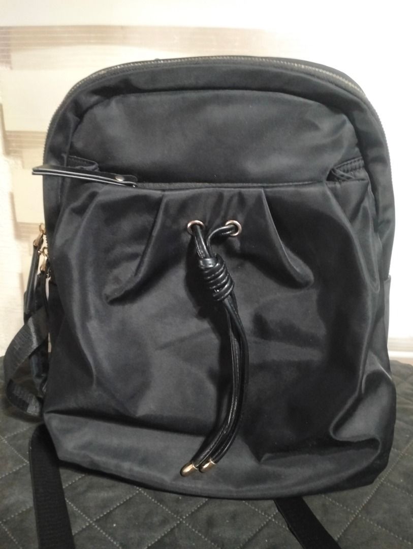CLN Black Backpack (Category: Backpacks) located in Cavite. Submitted by brightfire.b90615 (Listing ID 1465665302, Image 1). Description: - Main compartment with sturdy zippers, front zipped pocket, and drawstring detail with knots - Adjustable shoulder straps and top carry handle - Condition: Fully functional with normal signs of handling; notable wear and scuffing on the top leather handle, and slight fraying along the zipper fabric tracks.