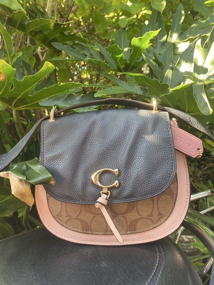 Coach Colorblock Saddle Bag (Category: Luxury Bags & Wallets) located in Manila. Submitted by cdb_22 (Listing ID 1465596552, Image 1). Description: - Authentic Coach crossbody saddle bag - Stylish mix of signature monogram canvas, dark grey pebbled leather, and pale pink trim - Elegant gold hardware with iconic C clasp and cute leather tie closure - Features an adjustable shoulder strap for customized comfort - Includes a matching pink Coach hang