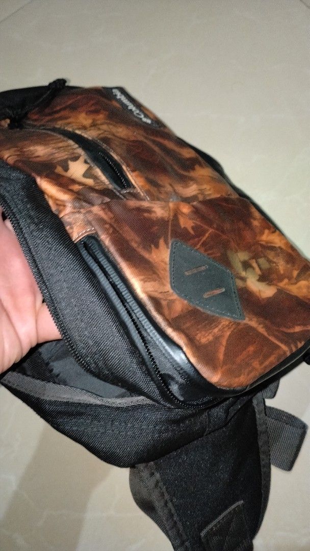 Columbia Camouflage Sling Bag Preloved (Category: Sling Bags) located in Polomolok. Submitted by lastthrift (Listing ID 1465636444, Image 3). Description: - Brand: Columbia - Design: Autumn leaf camo pattern with black accents - Material: Durable polyester - Features: Multiple interior and exterior compartments, sturdy zippers, and adjustable strap - Condition: Tag still attached inside with Japanese text - Perfect for: Everyday use and hands-fre