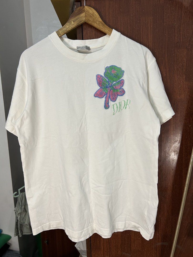 Dior White T-Shirt with Embroidered Rose Patch (Category: Shirts) located in Davao. Submitted by ruggedthrift444 (Listing ID 1465687004, Image 1). Description: - Authentic Dior t-shirt made in Italy - 100% premium cotton for maximum comfort - Features a colorful textured rose patch with green embroidered Dior lettering - Classic crew neck and short sleeves - Standard relaxed fit - Neck tag and interior care labels clearly attached - Condition: Br