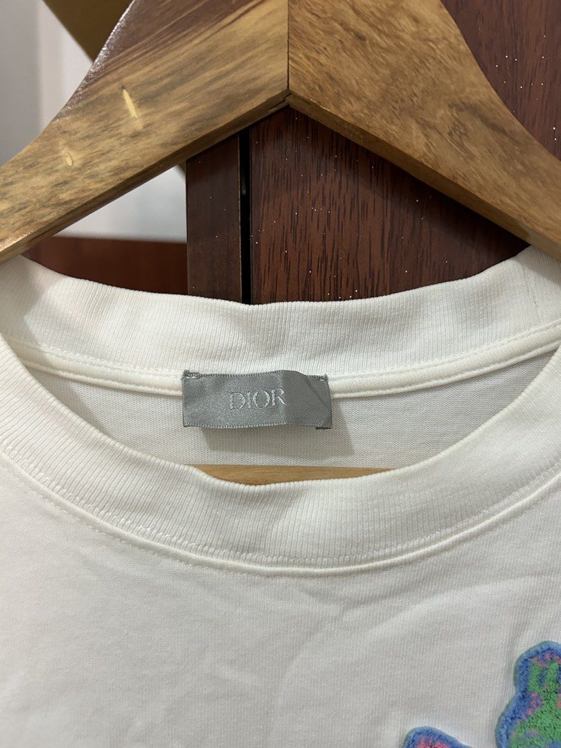 Dior White T-Shirt with Embroidered Rose Patch (Category: Shirts) located in Davao. Submitted by ruggedthrift444 (Listing ID 1465687004, Image 3). Description: - Authentic Dior t-shirt made in Italy - 100% premium cotton for maximum comfort - Features a colorful textured rose patch with green embroidered Dior lettering - Classic crew neck and short sleeves - Standard relaxed fit - Neck tag and interior care labels clearly attached - Condition: Br