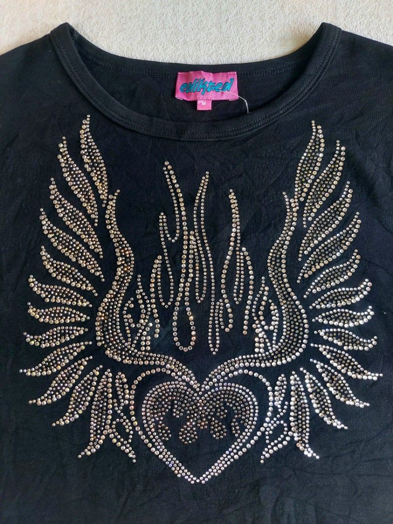 Edikted Black Rhinestone Crop Top Size M (Category: Sleeveless) located in Palayan City. Submitted by akhai420 (Listing ID 1465596889, Image 2). Description: - Brand: Edikted - Size: M - Style: Short sleeve crewneck crop top - Details: Rhinestone graphic featuring a heart, wings, and flame design; pink collar tag with blue text - Material: Soft cotton fabric.