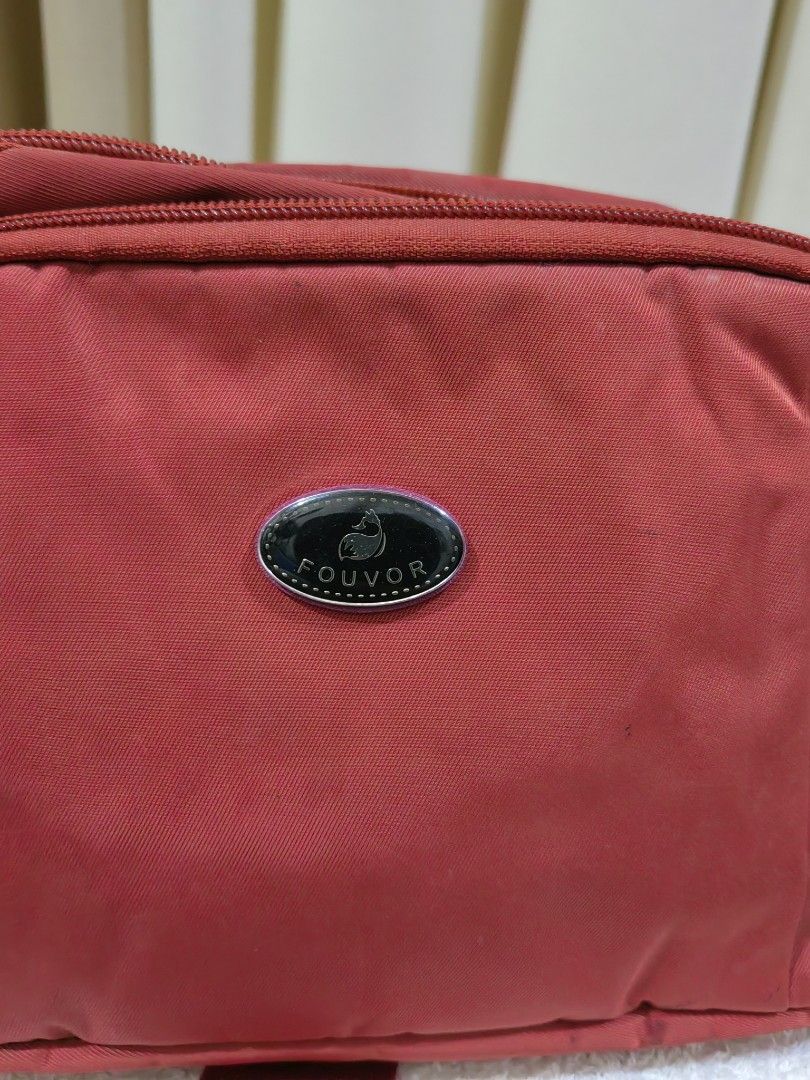 Fouvor Red Crossbody Bag (Category: Cross-body Bags) located in Makati City. Submitted by prelovedtreatedwithlove (Listing ID 1465622067, Image 2). Description: - Brand: Fouvor - Color: Vibrant red with sleek silver hardware - Design: Multiple zippered compartments with front oval logo plate - Interior: Clean black lining featuring extra slip pockets for organization - Strap: Adjustable red strap for a customized, comfortable fit - Condition: goo