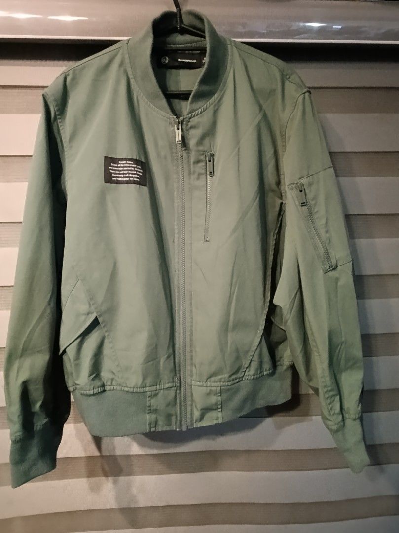 GU x UNDERCOVER Bomber Jacket Olive Green Size S (Category: Coats, Jackets and Outerwear) located in Manila. Submitted by yunicool (Listing ID 1465593643, Image 1). Description: - Brand: GU x UNDERCOVER - Item: Olive green bomber jacket - Size: S - Details: Full zip front, sleeve zip pocket, and vertical chest pocket - Design: Woven 'Kosmik Noise. Erase all the noise inside you...' patch on right chest - Finishing: Ribbed collar, cuffs, and hem -