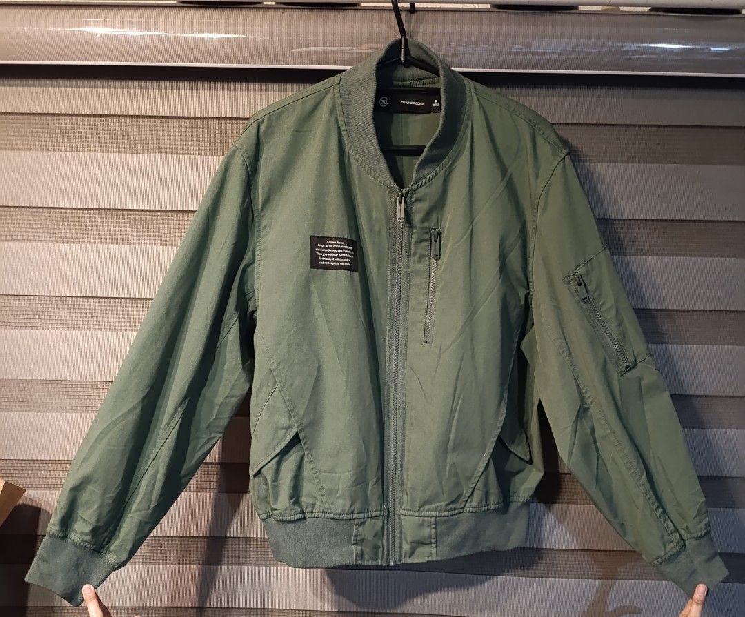 GU x UNDERCOVER Bomber Jacket Olive Green Size S (Category: Coats, Jackets and Outerwear) located in Manila. Submitted by yunicool (Listing ID 1465593643, Image 3). Description: - Brand: GU x UNDERCOVER - Item: Olive green bomber jacket - Size: S - Details: Full zip front, sleeve zip pocket, and vertical chest pocket - Design: Woven 'Kosmik Noise. Erase all the noise inside you...' patch on right chest - Finishing: Ribbed collar, cuffs, and hem -