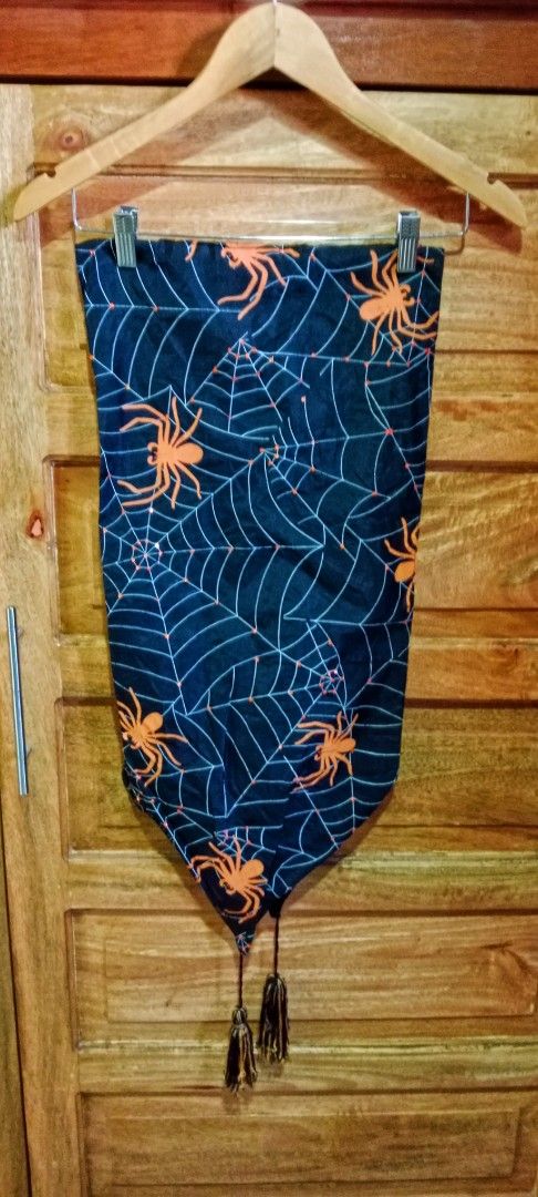 Halloween Spider Web Table Runner with Tassels (Category: Table Linen & Textiles) located in Mangaldan. Submitted by closetqwin (Listing ID 1465635744, Image 1). Description: 55 inches Length -Black with orange spider - Details: Pointed ends finished with black and orange tassels.