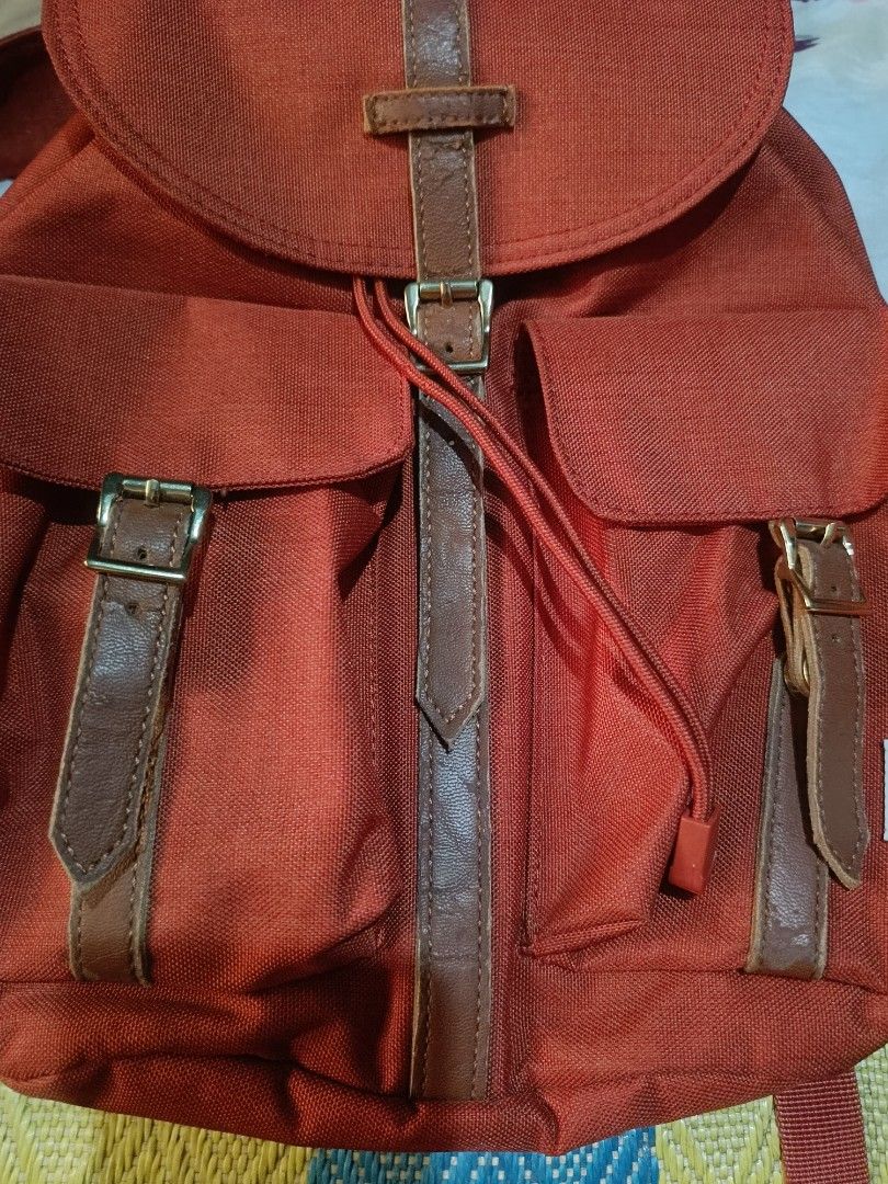 Herschel Dawson (Category: Backpacks) located in Urdaneta. Submitted by tetsudoubletaps (Listing ID 1465666419, Image 3). Description: + SF Goods na goods pa yung tela as in, natambak lang kaya mejo may cracks sa leather pero minimal. - Brand: Herschel - Color: Vibrant red with contrast brown faux leather straps and sturdy metal hardware - Storage: Main compartment with secure drawstring cinch and flap top, two front buckle pockets, and an interi