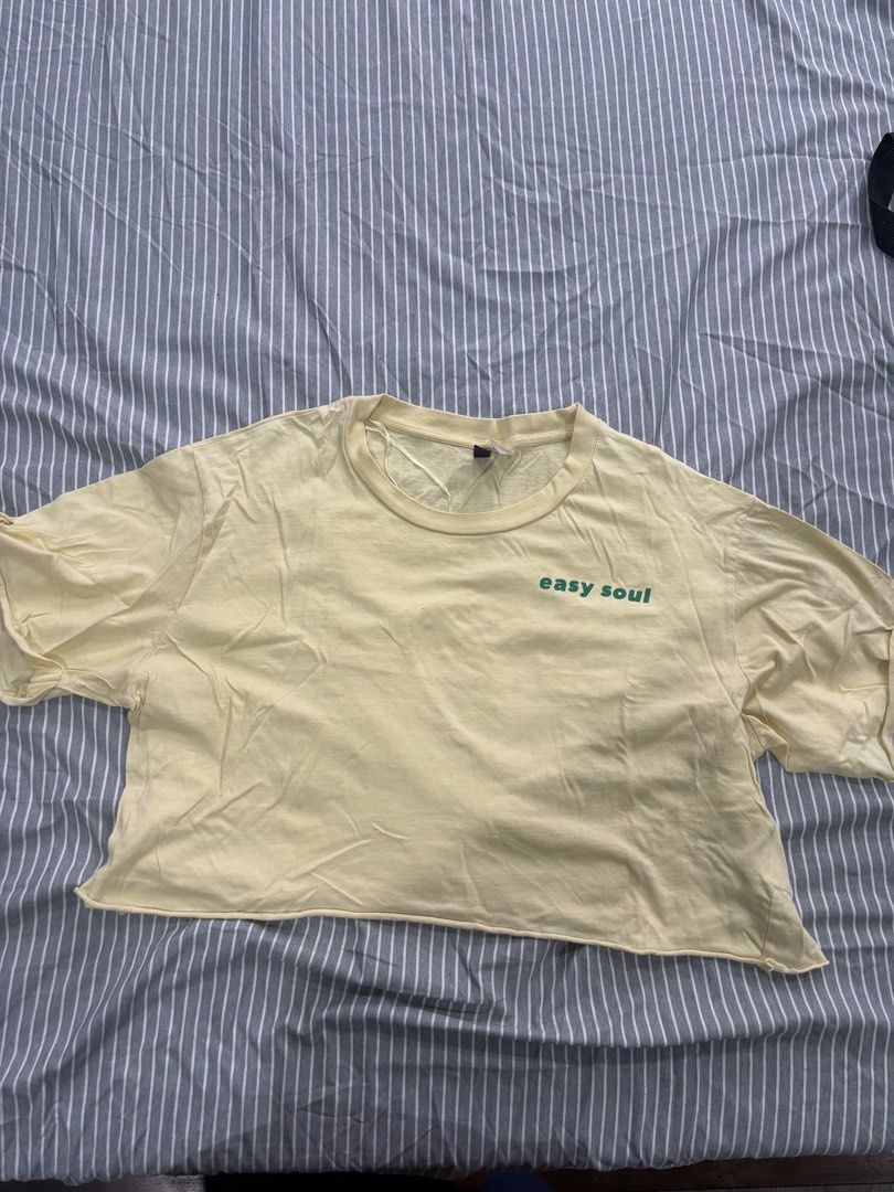 H&M Cropped Shirt (Category: Sleeveless) located in San Pablo. Submitted by loved.goods0501 (Listing ID 1465642670, Image 1). Description: Color: Light yellow with green 'easy soul' front text Fit: Relaxed crop top style Details: Round neckline and trendy raw hem finish.