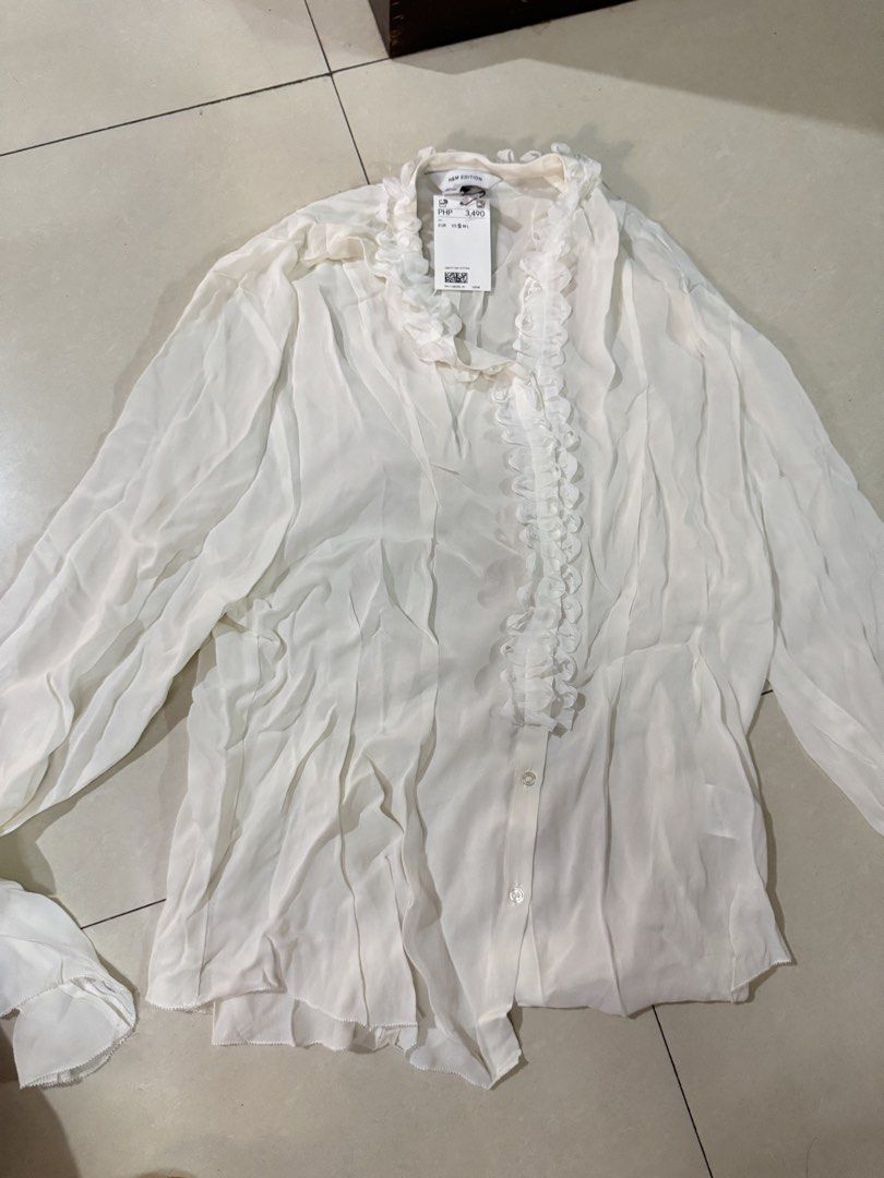 H&M Edition White Ruffle Blouse (Category: Blouses) located in Quezon City. Submitted by sweetlyluxe (Listing ID 1465622718, Image 1). Description: - Brand: H&M Edition - Condition: Brand new with tags (never worn) - Color: White - Details: Delicate ruffle trim along the front placket and neckline, long sleeves, button-up front - Fabric: Lightweight sheer - Original Price: 3,490 PHP - cottagecore, pirate costume, whimsy, halloween.