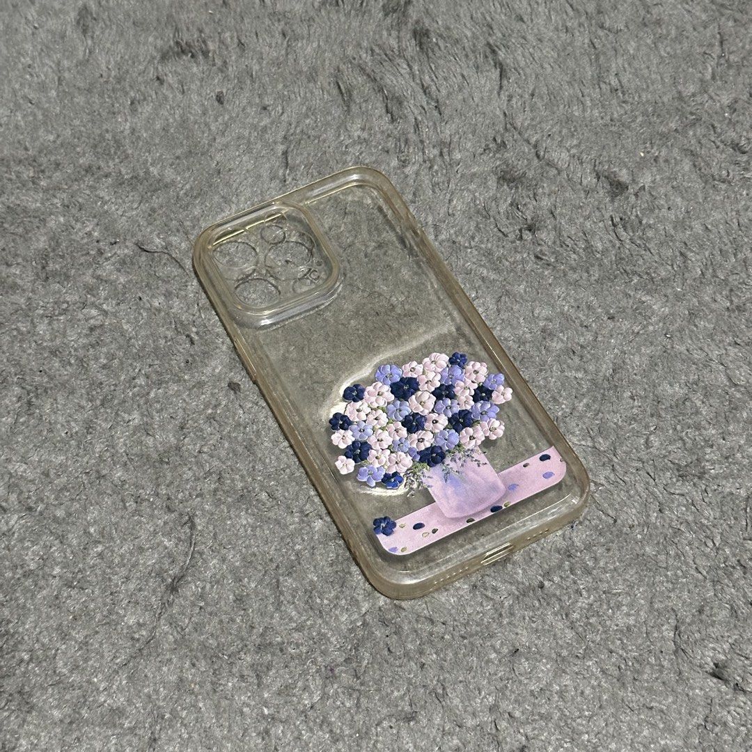 Iphone 14 Pro Max Phone Case (Category: Cases & Sleeves) located in Lipa City. Submitted by jecoparra (Listing ID 1465699784, Image 2). Description: - Compatible model: iPhone 14 Pro Max - Design: Clear transparent case with a purple and blue floral bouquet graphic at the lower back - Material: Clear plastic/TPU - Condition: Pre-owned, well-maintained - Features: Slim profile, shows original phone color while adding a stylish touch.