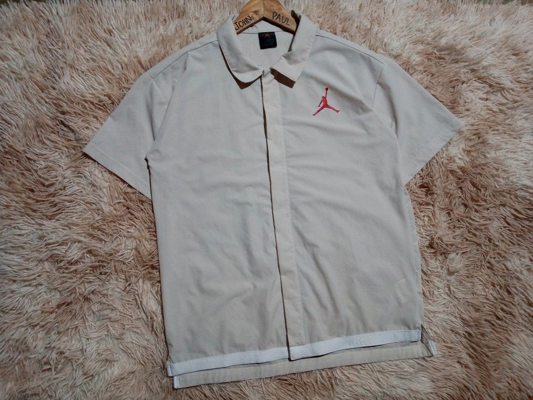 Jordan Short Sleeve Button-Up Shirt (Category: Tshirts & Polo Shirts ) located in Boston. Submitted by johnpaulvi30029 (Listing ID 1465692760, Image 3). Description: - Authentic Jordan short sleeve button-up shirt in beige - Features snap front closure and classic collar - Red Jumpman logo on left chest with large black and red Jordan lettering on the back - Stylish white striped trim along the bottom hem - DM for measurements or more details, tr
