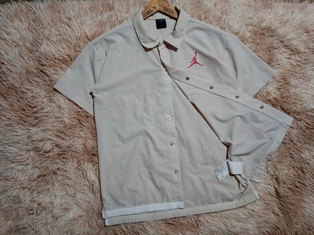 Jordan Short Sleeve Button-Up Shirt (Category: Tshirts & Polo Shirts ) located in Boston. Submitted by johnpaulvi30029 (Listing ID 1465692760, Image 1). Description: - Authentic Jordan short sleeve button-up shirt in beige - Features snap front closure and classic collar - Red Jumpman logo on left chest with large black and red Jordan lettering on the back - Stylish white striped trim along the bottom hem - DM for measurements or more details, tr